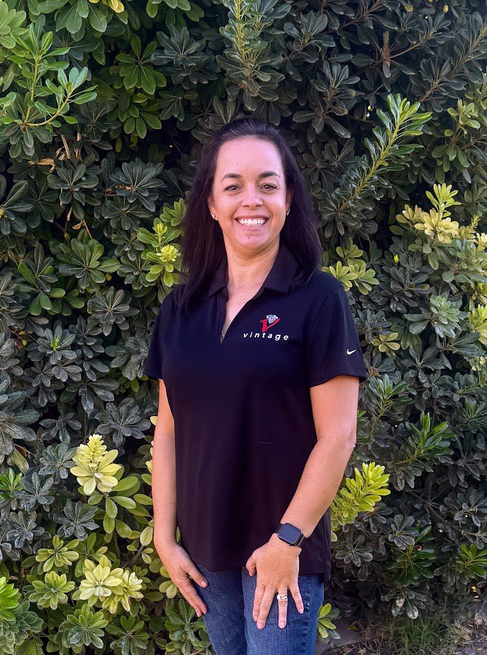 Woman smiling in front of green foliage.